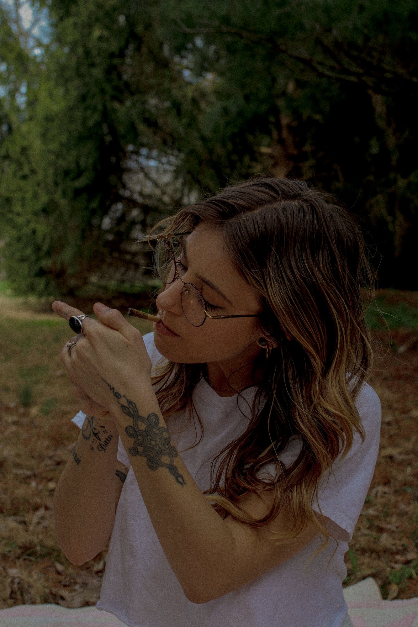 Woman with tattoos and glasses sitting outdoors in a natural setting