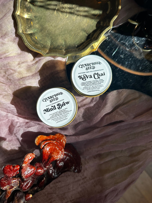 Two jars labeled 'Conscious Seed' on a fabrics with a vintage brass plate, mirror and cultivated Reishi mushroom.