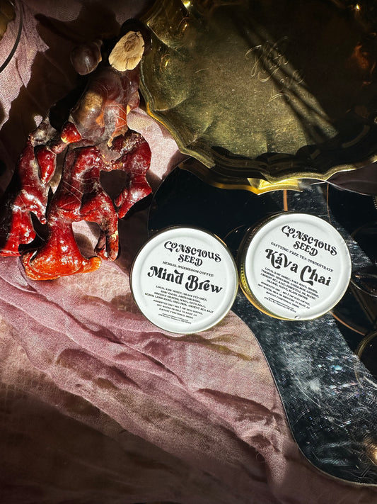 Two jars labeled 'Conscious Seed' on a fabrics with a vintage brass plate, mirror and cultivated Reishi mushroom.