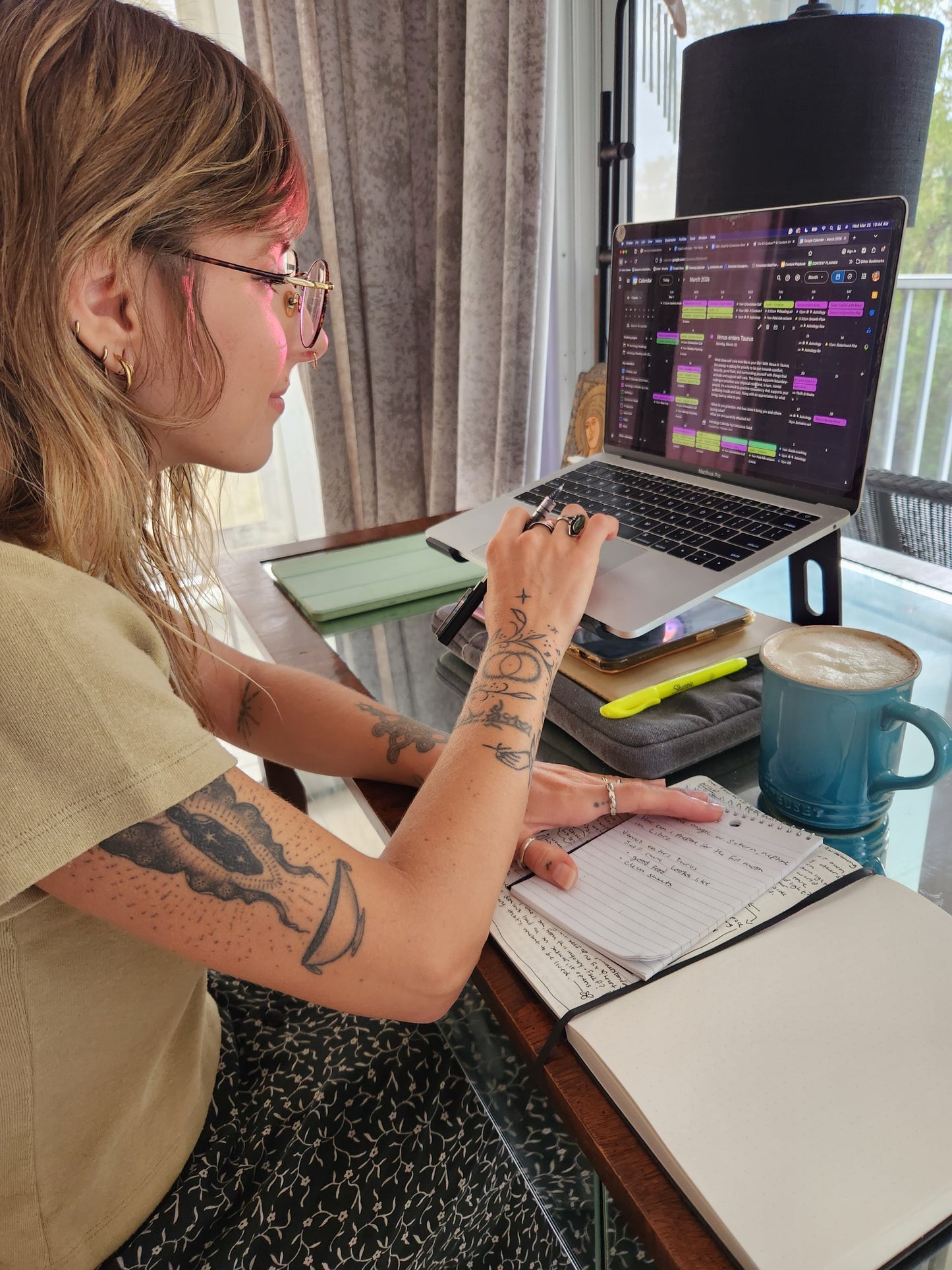 Working on a laptop at a desk with a notebook and coffee cup checking the Digital Astrology Calendar by Conscious Seed